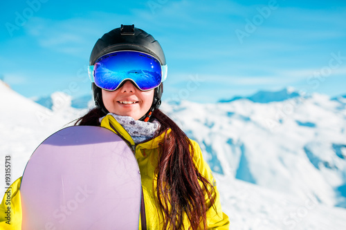Photo of smiling woman in helmet and mask with snowboard on background of snowy hills