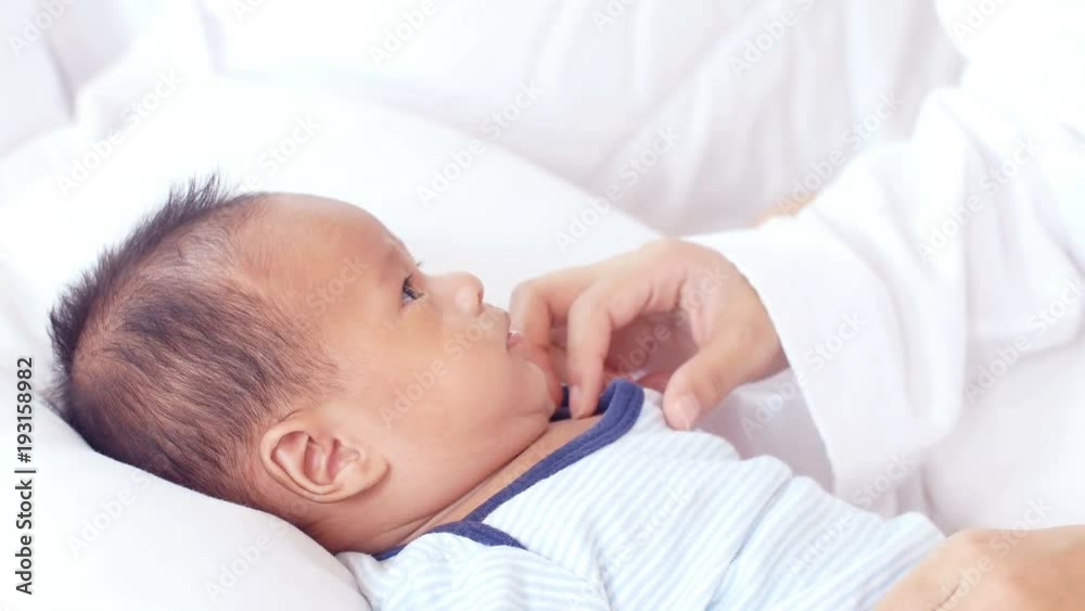 Cute baby lies on bed. Mother kiss her baby on bed. 