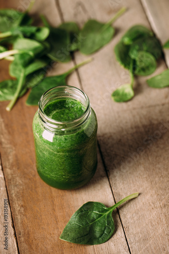 Green spinach juice jar on a rustic wooden table and spoon
