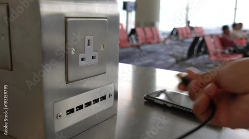 Traveler charging mobile phone battery at free service charging station at International Airport. Free battery charging station in the airport terminal for traveler.
