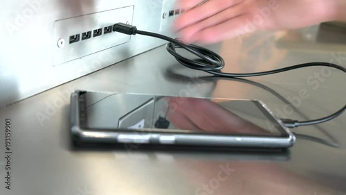 Traveler charging mobile phone battery at free service charging station at International Airport. Free battery charging station in the airport terminal for traveler.