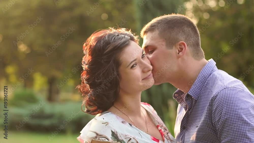 Close-up of a young attractive couple is kissing at sunset. Close-up portrait of young kissing couple at sunshine. Slow motion. Close-up of a young attractive couple is kissing at sunset. Close-up portrait of young kissing couple at sunshine. Slow motion.