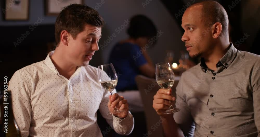 4K Attractive smart-casual men chatting over a glass of wine in fine restaurant, could be friends or business colleagues.