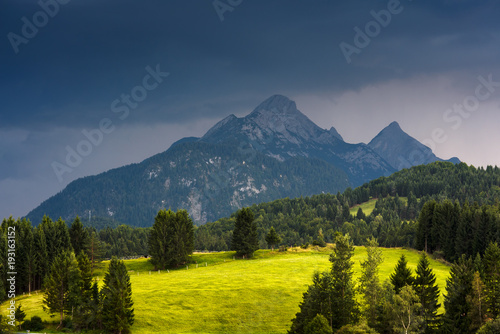 Sunlit bright meadow against mountain and thundercloud