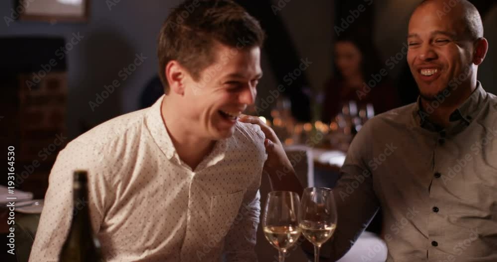 4K Attractive smart-casual men chatting & laughing over a glass of wine in restaurant, could be friends or business colleagues.. Slow motion