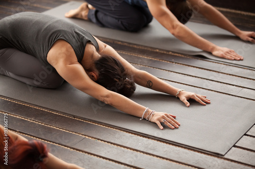 Group of young sporty people practicing yoga lesson with instructor, stretching in Child exercise, Balasana pose, working out, indoor, studio, close up photo