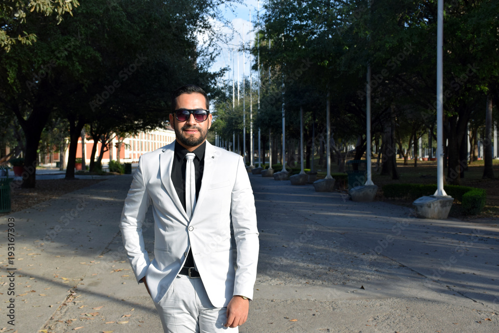 smiling young businessman with shades standing in a park