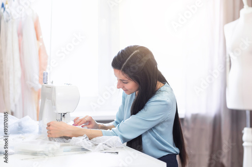 Close-up portrait of young indian seamstress or dressmaker sews on sewing machine in her own workplace. Sewing hobby  small business or startup concept