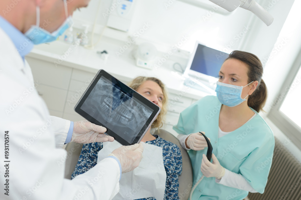 dentist with teeth x-ray on tablet and patient