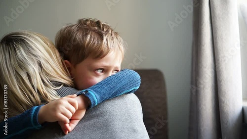 Upset little boy hugging his mother at home