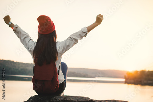Happy Asian woman sitting on rock in nature during sunset, Relax time on holiday concept travel,selective and soft focus,color of hipster style