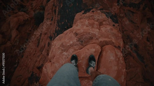 Looking Down at Feet Walking on Narrow Rocky Cliff above Canyon
