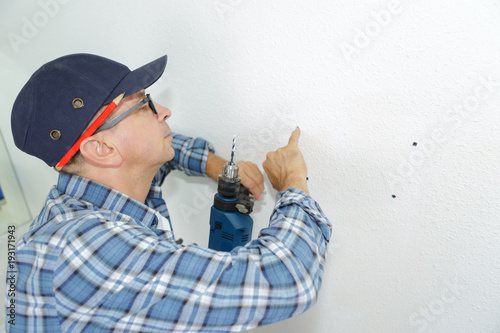 seniro man drilling a hole in a wall photo