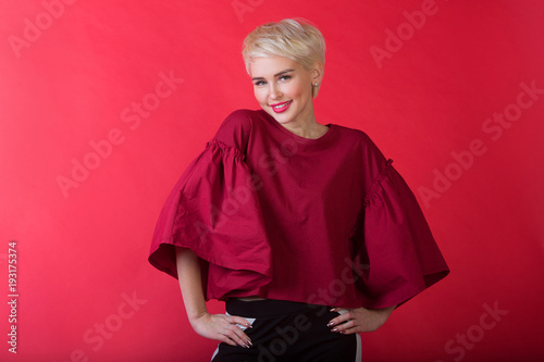 beautiful young girl with snow-white smile and healthy teeth with short hairdo on red background