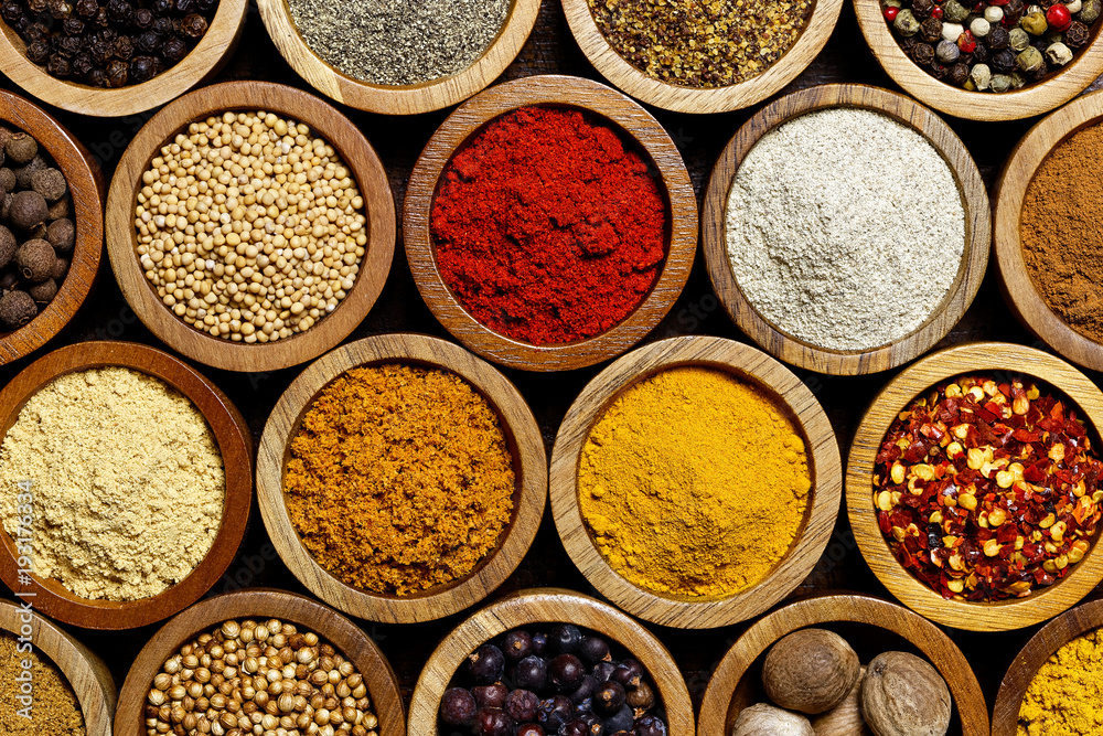 Background of arranged spices in small wood bowls from above.