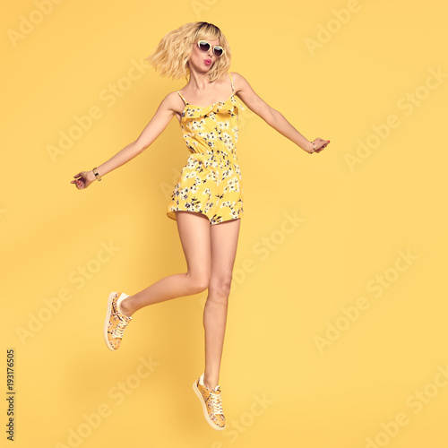 Happy girl Jumping in Studio on Yellow background. Blond Slim Model Having Fun in Fashionable Sunglasses, Trendy Summer Playsuit . Young Playful Beautiful woman in Stylish fashion Outfit