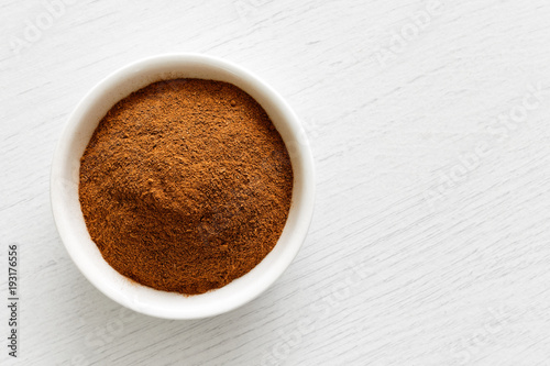 Finely ground cinnamon in white ceramic bowl isolated on white wood background from above. photo