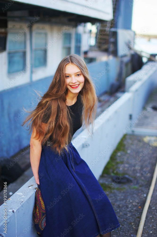 Portrait of young beautiful smiling cheerful girl with long hair while walking on the waterfront a blurred pier background. Activity holiday, healthy lifestyle.