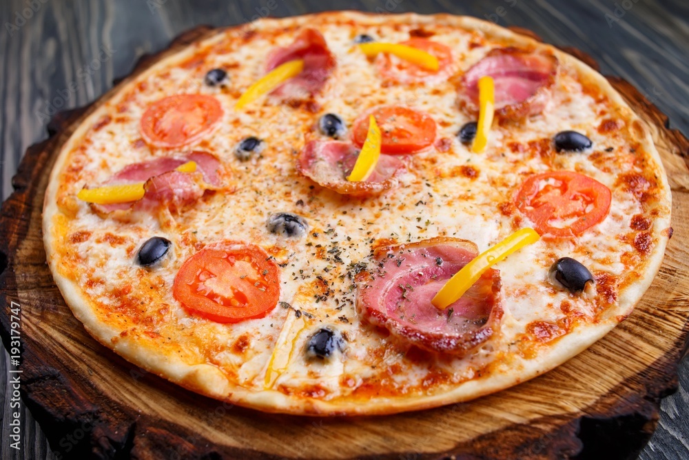 Appetizing sicilian pizza with bacon, olives and tomatoes served on wood. Italian food, restaurant or pizzeria concept