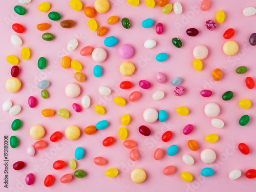 Many scattered colorful sweets, candies, lollipops on  bright pink background, top view