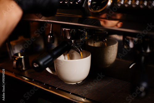 Barista poring / making coffee latte at coffee machine. Close-up barista preparing cappuccino.