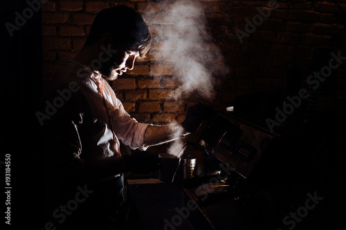 Close-up image of barista man using coffee-making machine to steam milk in cafe.