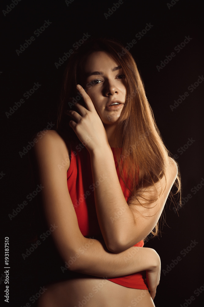 Tender young woman with long shiny hair posing at the black background