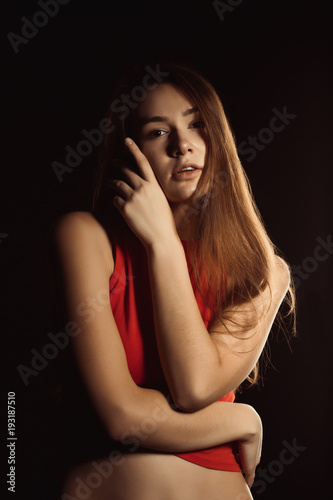 Tender young woman with long shiny hair posing at the black background