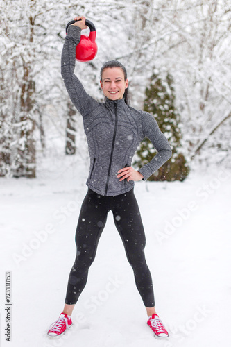 Happy young woman holding kettlebell in snow