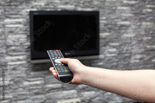 Human hand turning on flat tvset hanging on wall in room