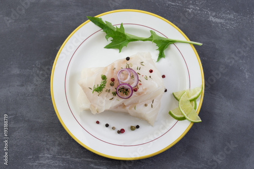 Fresh raw cod fish fillet on a plate with parsley and lemon isolated on grey slate background photo