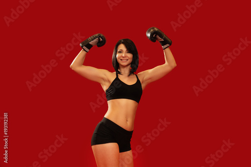  Woman celebrating victory with arms up wearing boxing gloves on red background.