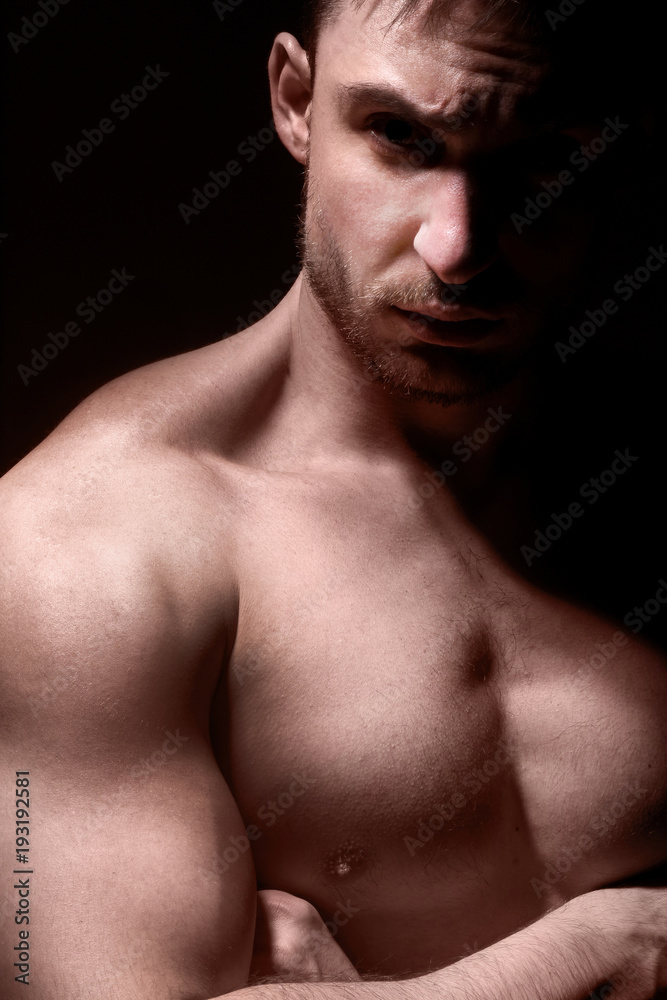 Big and strong muscular man in posing in a low light. Fitness model or a trainer showing his biceps, shoulders and chest. Angry mma fighter or a Bodybuilder is ready to kick ass. Big and strong muscular man in posing in a low light. Fitness model or a trainer showing his biceps, shoulders and chest. Angry mma fighter or a Bodybuilder is ready to kick ass.