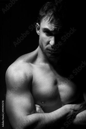 Big and strong muscular man in posing in a low light. Fitness model or a trainer showing his biceps, shoulders and chest. Angry mma fighter or a Bodybuilder is ready to kick ass.