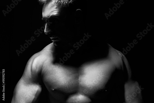 Big and strong muscular man in posing in a low light. Fitness model or a trainer showing his biceps, shoulders and chest. Angry mma fighter or a Bodybuilder is ready to kick ass.