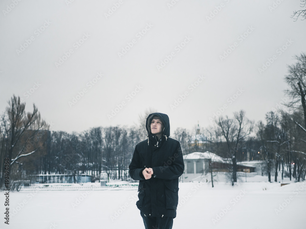 young man in the hood standing outside on a snowy winter day young man in the hood standing outside on a snowy winter day