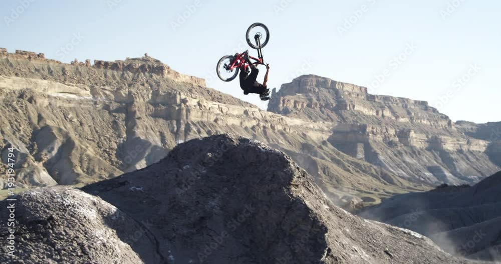 Slow motion, mountain biker does backflip off jump in Utah canyon