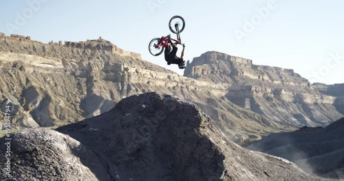 Slow motion, mountain biker does backflip off jump in Utah canyon