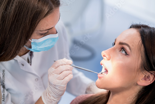 people  medicine  stomatology and health care concept - happy female dentist with mirror checking patient girl teeth up at dental clinic office while male assistant is waiting behind.