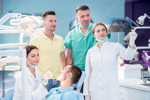 Dental medical team examining and working on young male patient.Dentist s office  while technician is reviewing xray.