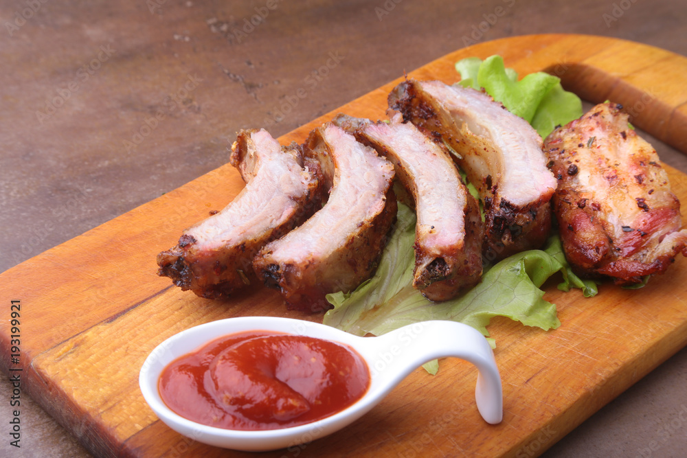 grilled barbecued ribs with lettuce leaves, hot chili pepper and sauce on wooden cutting board. grilled barbecued ribs with lettuce leaves, hot chili pepper and sauce on wooden cutting board.