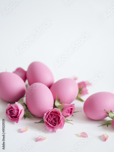 Easter greeting card with Easter eggs and pink roses on white background with copy space.