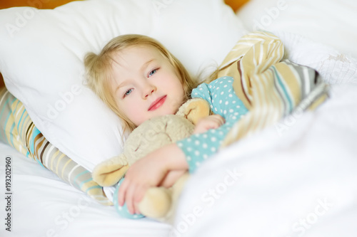Adorable little girl sleeping in the bed with her toy. Tired child taking a nap under white blanket.