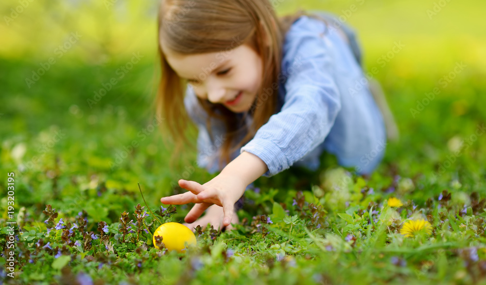 © MNStudio - Adorable little girl hunting for Easter egg in blooming spring garden on Easter day