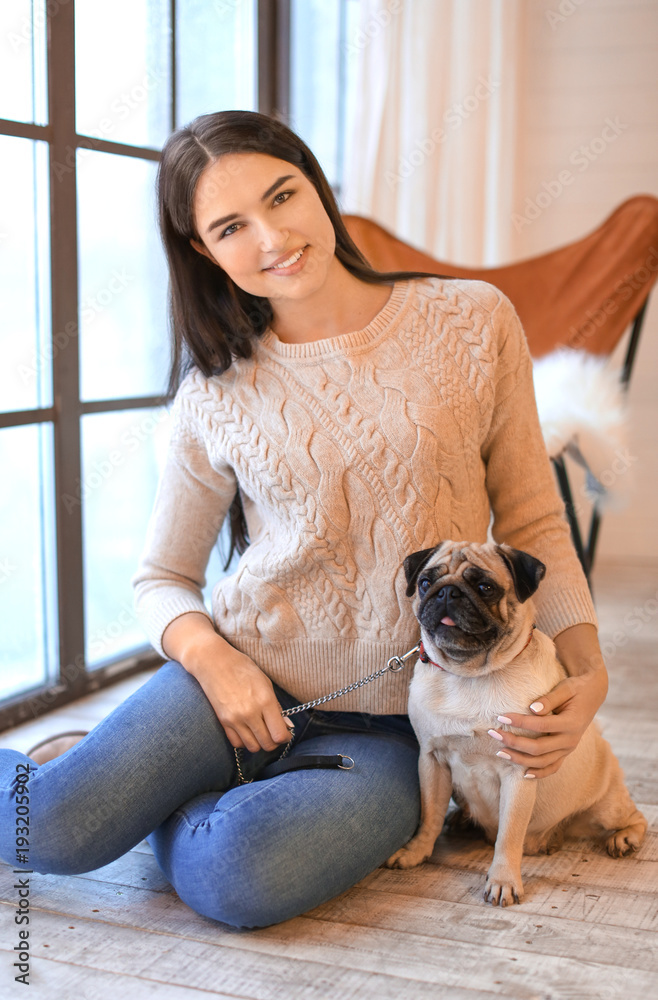 Young woman with cute pug dog near window at home. Pet adoption Young woman with cute pug dog near window at home. Pet adoption