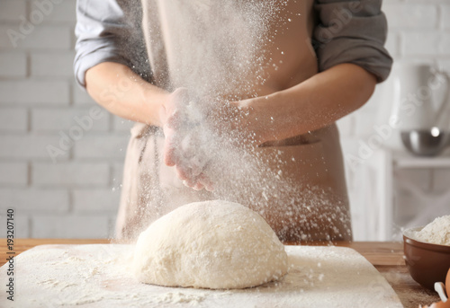Woman clapping and sprinkling flour over dough on table