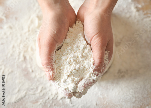 Woman holding wheat flour above table, closeup