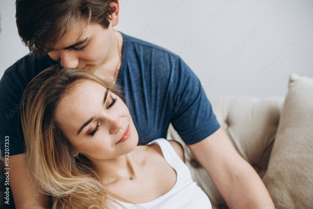 Gentle photo of a loving couple who hugs each other sitting on a sofa in a cozy bright room Gentle photo of a loving couple who hugs each other sitting on a sofa in a cozy bright room