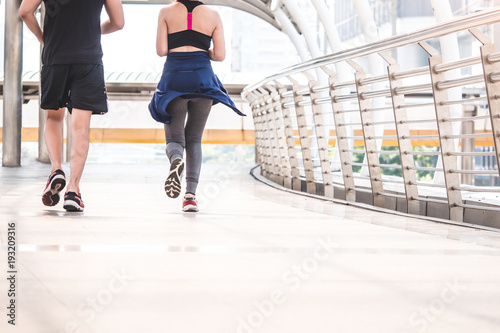 Young runners running on city bridge, Sporty couple jogging at morning with Bangkok urban scene background