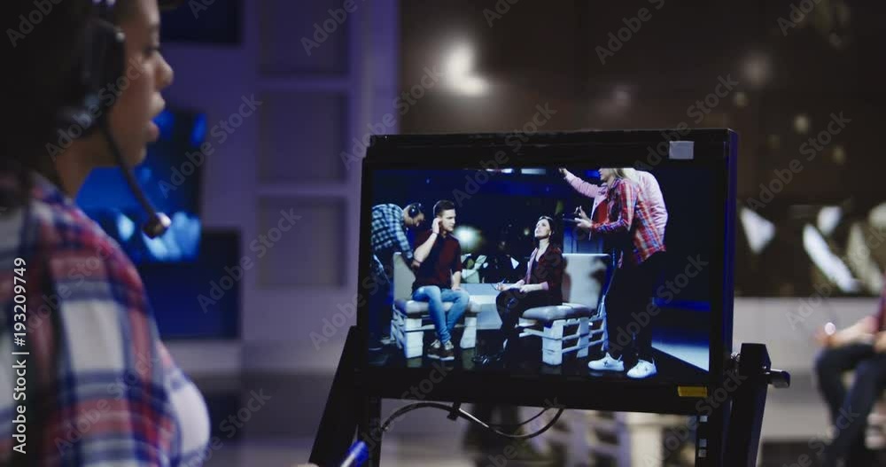 Casual African-American woman in headset controlling process of shooting TV show standing in front of computer screen and watching record.